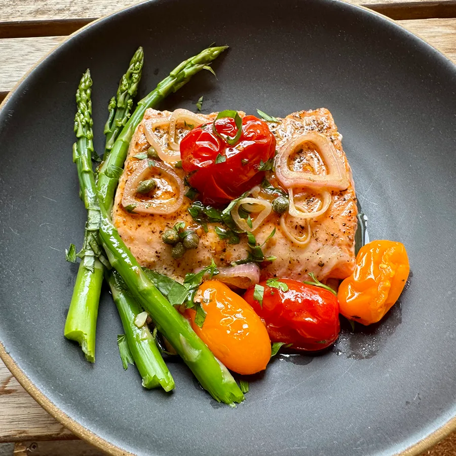 Seared salmon with burst tomatoes and asparagus on a dark plate